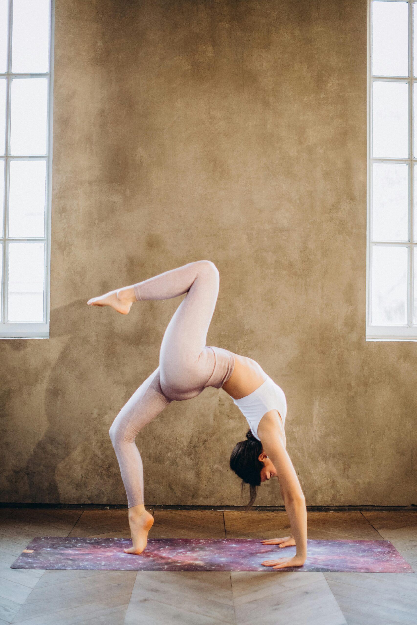 Woman performing a graceful wheel pose balancing on one leg in a bright yoga studio.