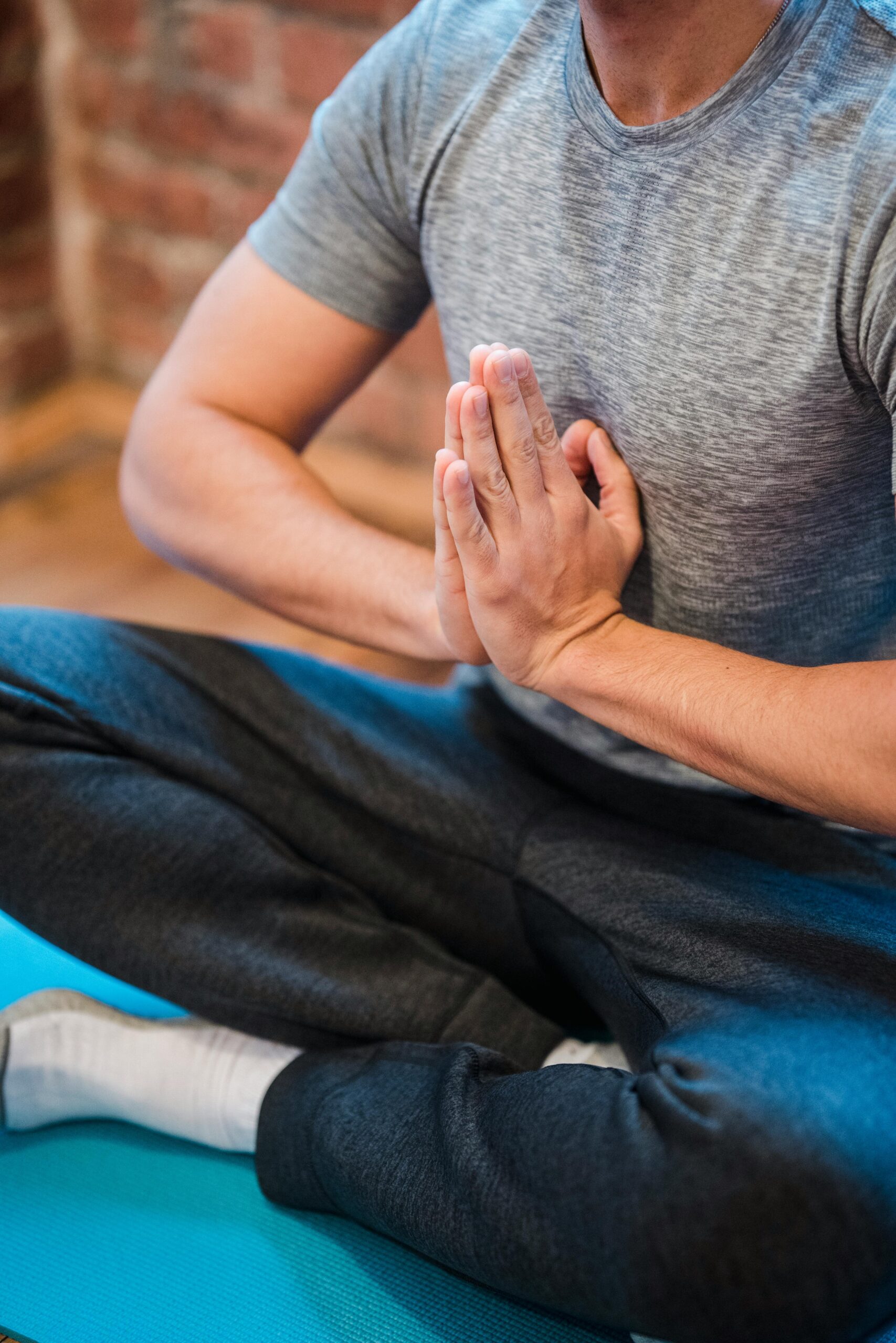 High angle of crop faceless male sitting with crossed legs in Sukhasana with praying hands on chest
